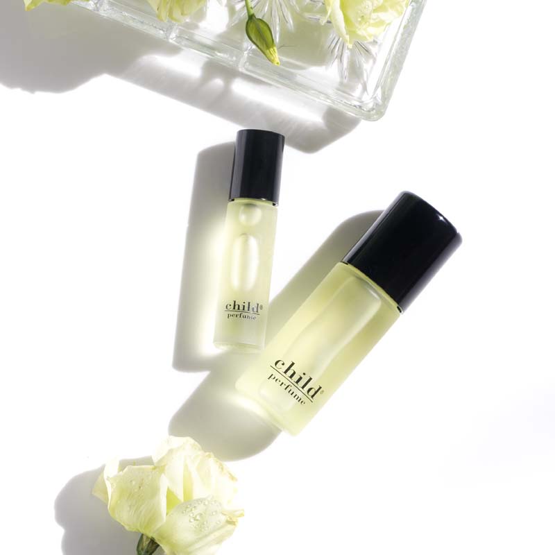 Beauty shot of Child Perfume Roll On with both size bottles with white flowers and white roses in the background