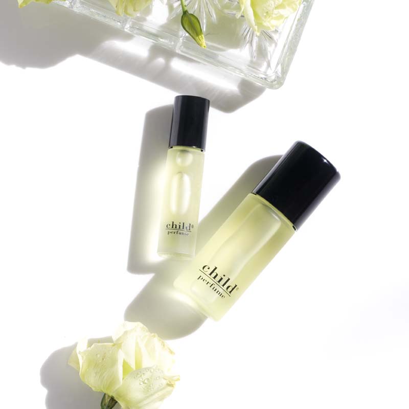 Beauty shot of Child Perfume Roll On with both size bottles with white flowers and white roses in the background