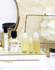 Lifestyle shot of a selection of Child Perfume products including Roll Ons, Limited Edition Spray, Travel Spray and Body Creme on vanity tray with white flowers and mirror in the background
