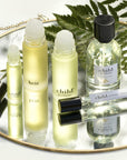 Lifestyle shot of a selection of Child Perfume products including Roll Ons, Limited Edition Spray and Travel Spray on mirrored vanity tray and fern branch in the background