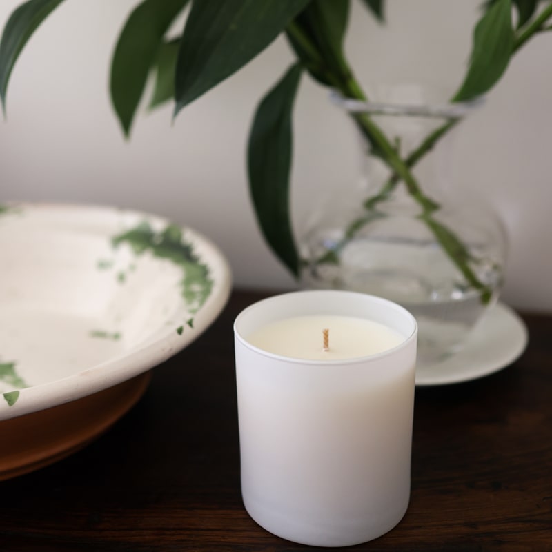 Lifestyle shot of Child Perfume Scented Candle 8 oz shown on wood table with dish and vase in the background