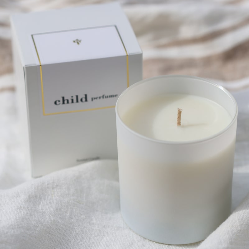 Lifestyle shot of Child Perfume Scented Candle 8 oz shown with box sitting on white linen fabric