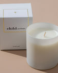 Lifestyle shot of Child Perfume Scented Candle 8 oz shown with box and tan background